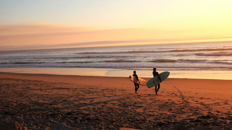 People walking down the beach for a sunset surf